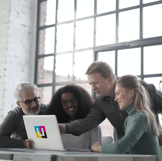 Four person team gathered around a laptop.
