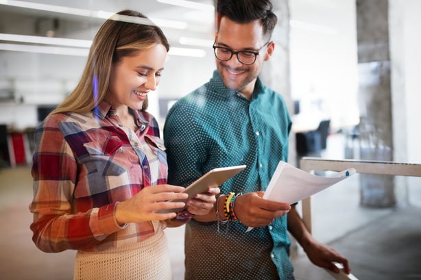 Two people looking at a tablet while one holds papers.