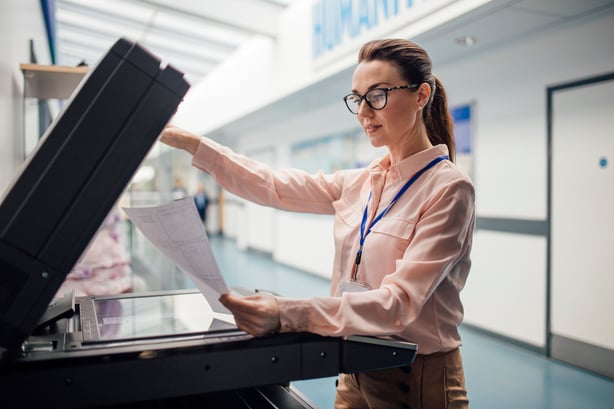 A person standing in front of a copier with papers in their hand.