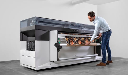 Person standing in front of printing machine, pulling out designed item.