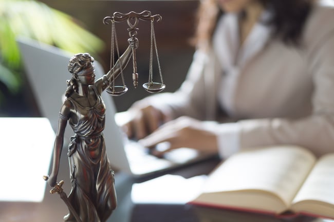 Person seated at desk with book, laptop, and Justice statue.