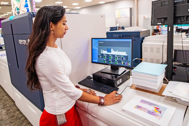 Person standing in front of computer near printed materials.