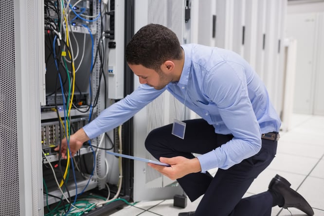 Man checking tablet pc as he is plugging cables into server in data center