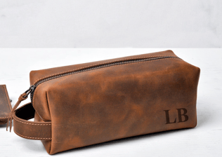 This image shows a brown leather toiletry bag with initials stamped on.