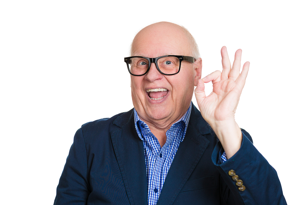 Closeup portrait, happy, cheerful, smiling, senior mature nerd man in black glasses, showing OK sign, isolated white background. Positive human emotions, facial expressions, feelings, attitude